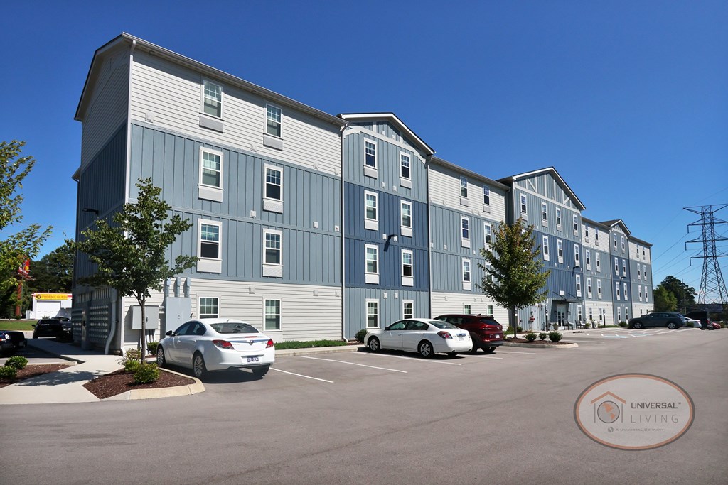 The rear of a large blue and grey apartment building with lush trees.