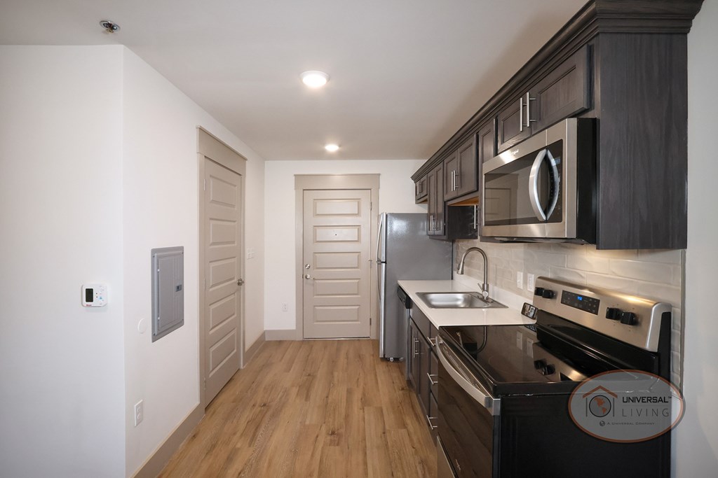 A kitchen with stainless steel appliances, dark cabinets, and hardwood vinyl flooring.