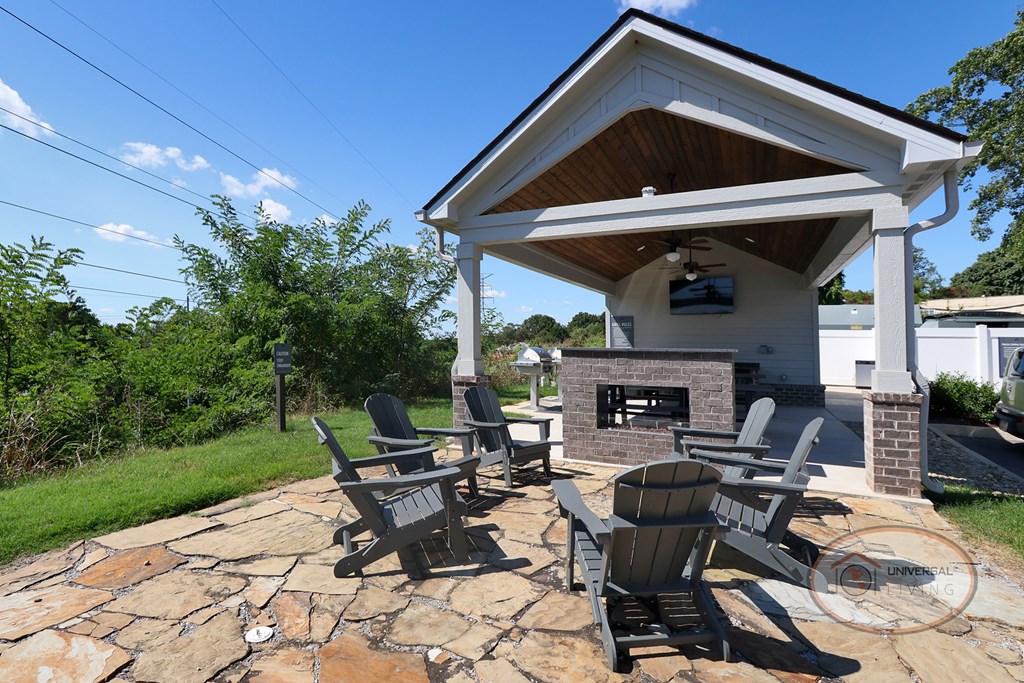An outdoor pavilion with lounge seating, fireplace, flat screen TV, picnic tables, and grills.