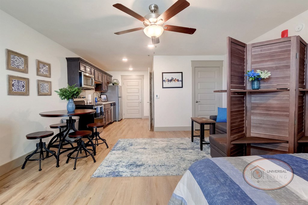 A studio apartment with hardwood vinyl flooring, white walls, dark cabinets, and a ceiling fan.