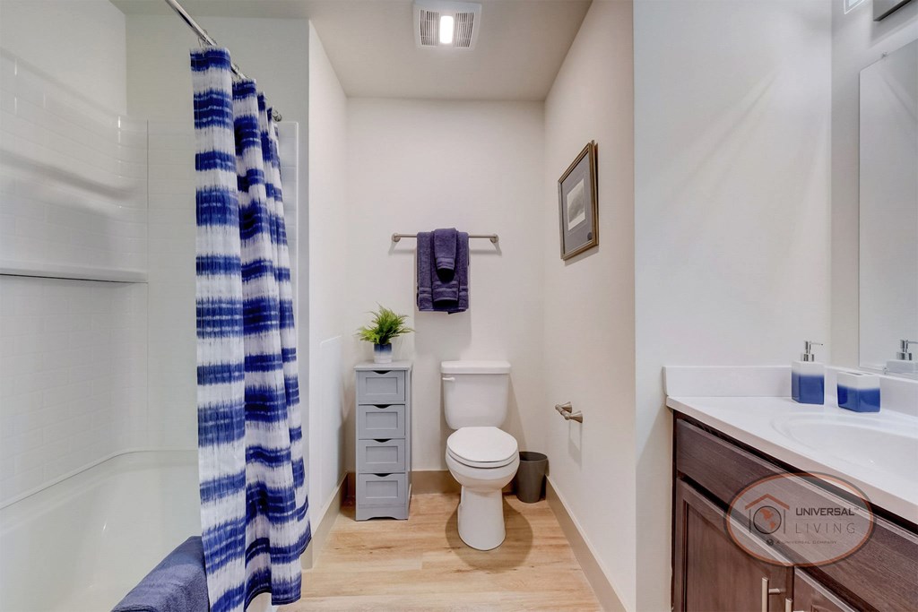 A bathroom with white walls, dark cabinets,  a toilet, sink, and shower.