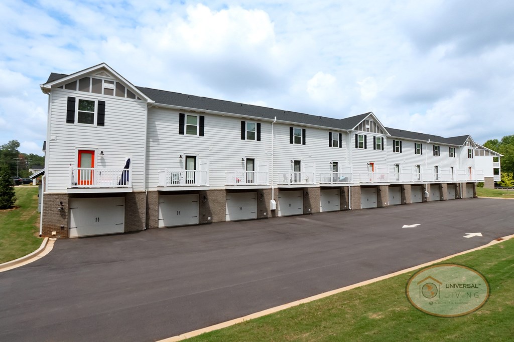 A white and grey apartment building from the rear with drive under garages and balconies.