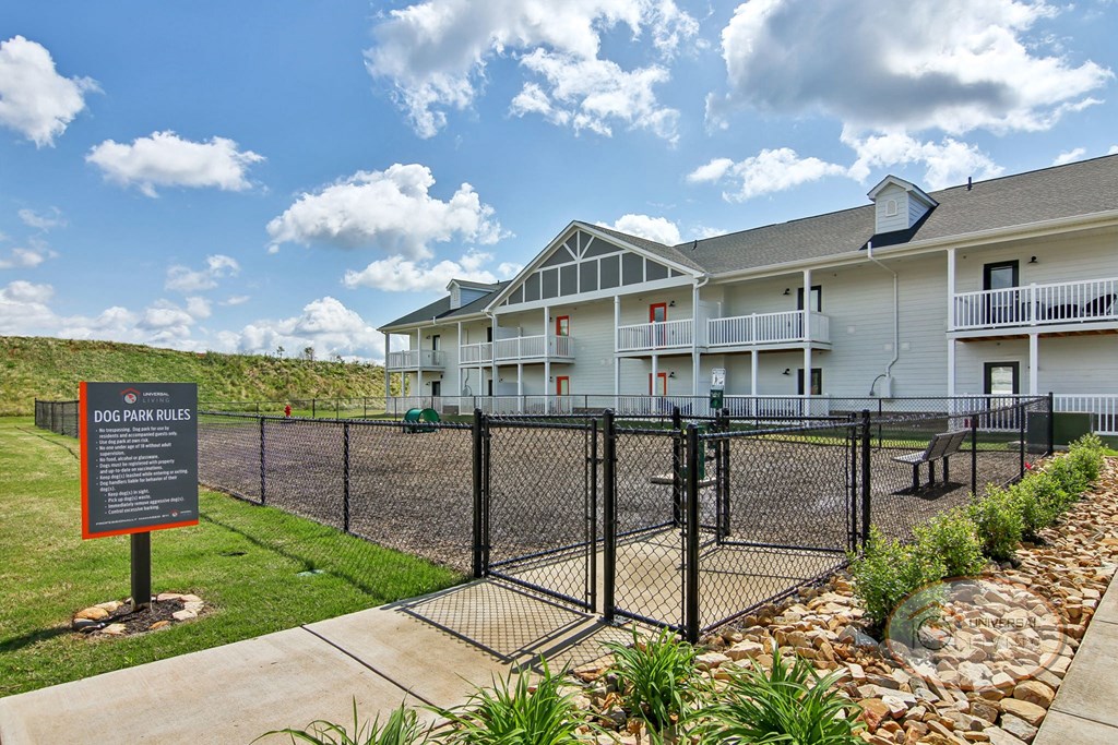 A fenced in dog park with an apartment building in the background.