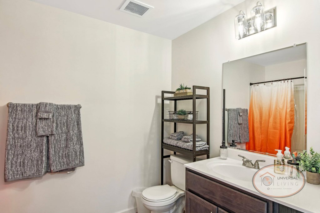 A bathroom with a toilet, sink, mirror, and a hanging coat.
