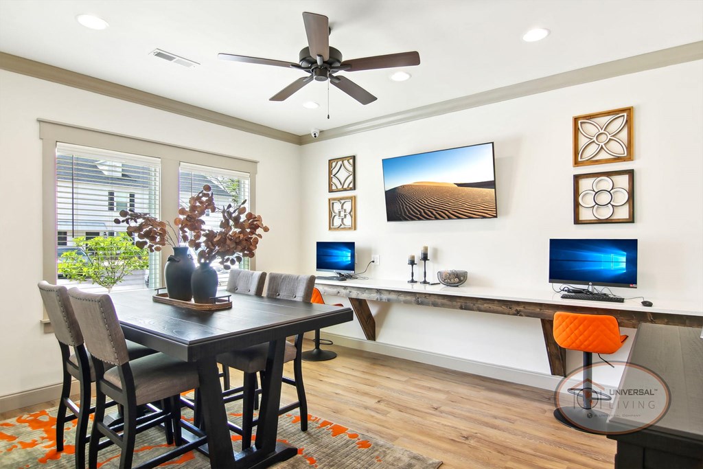 The business center with computers and bar stool seating, a table and chairs, and a flat screen TV.