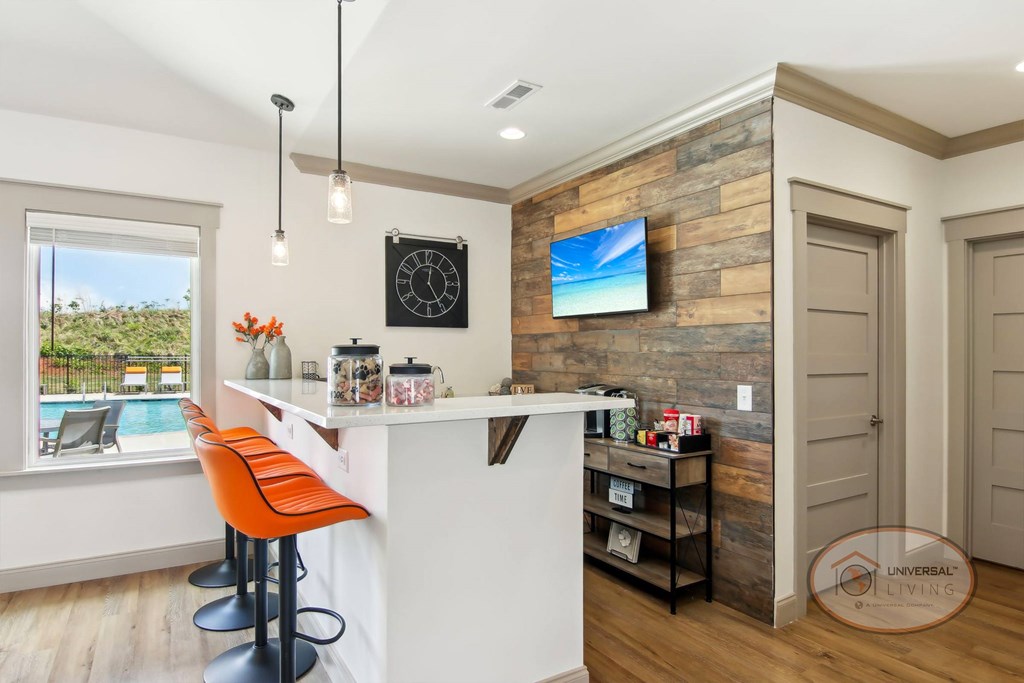 A coffee bar inside the clubhouse lounge with orange bar stool seating and a flat screen TV on a rock accent wall.