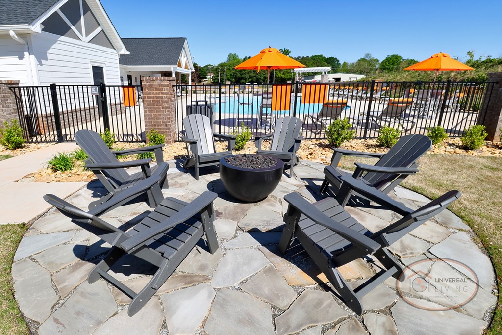 An outdoor fire pit surrounded by Adirondack chairs on a stone pad..