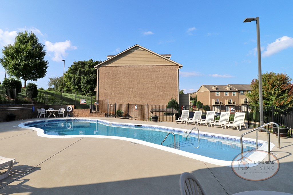 A swimming pool with lounge chairs and apartment buildings in the background.