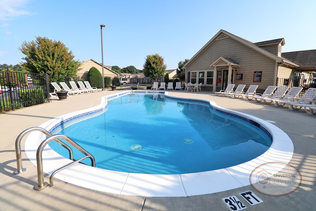 The Villas at Boone Ridge, Apartment Home Community in Johnson City, Tennessee. A swimming pool with lounge chairs in front of the property clubhouse.