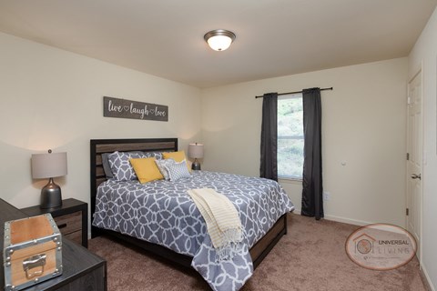 A bedroom with a large bed, large window, carpet, and white walls.
