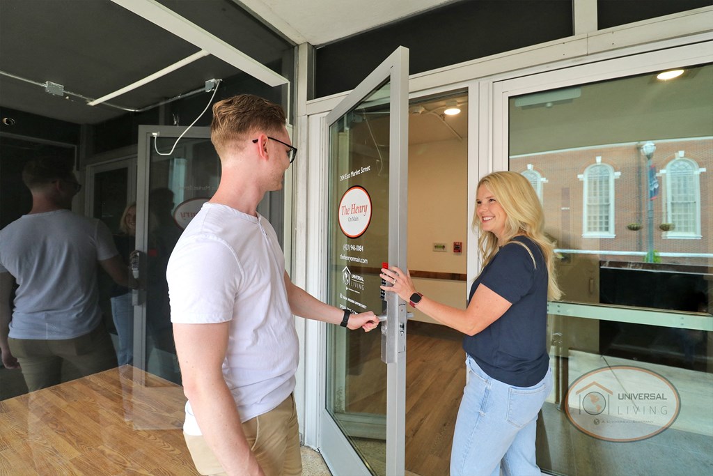 A man and woman walking through a glass door into The Henry on Main apartment home.