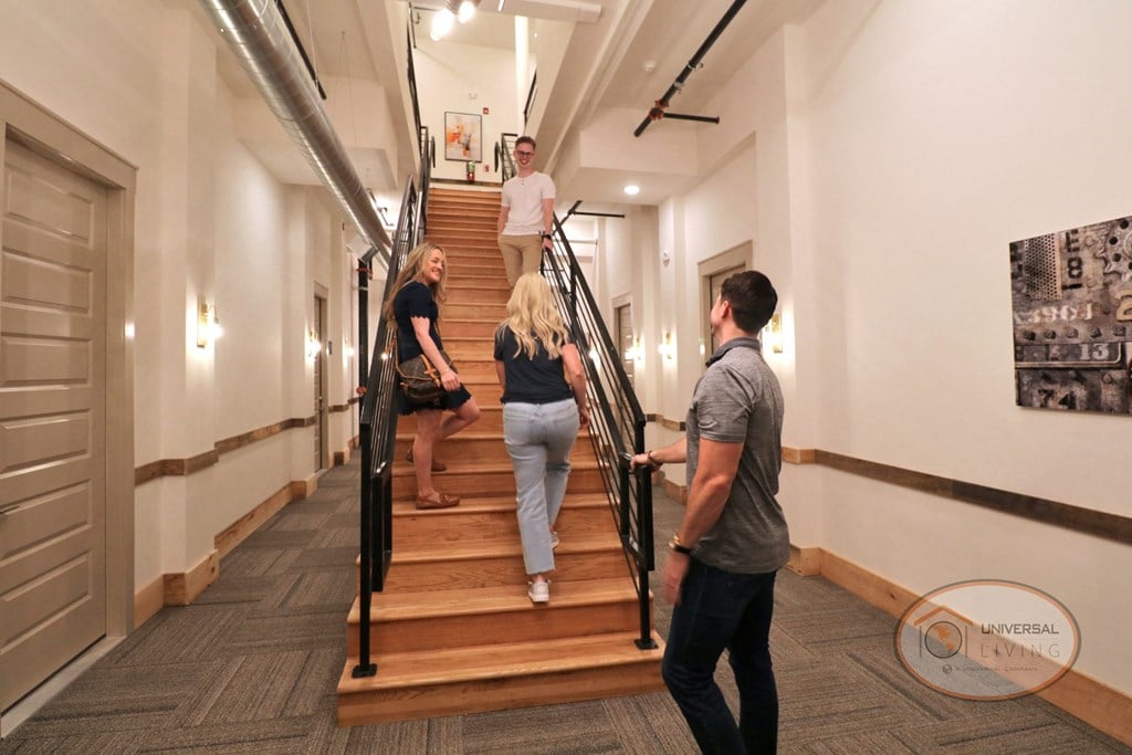 A group of happy people, walking up a brightly lit staircase to the third floor.
