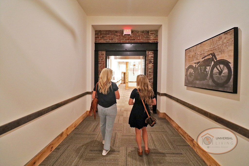 Two women walking down a hallway toward a brick passage.