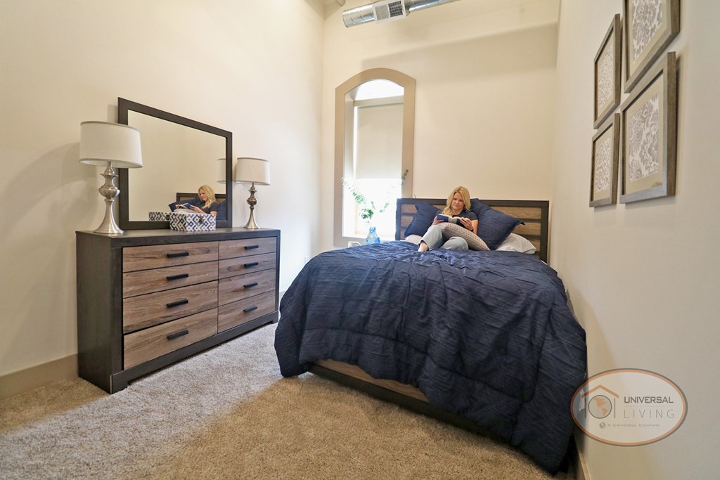 The Henry on Main, Apartment Homes in Downtown Johnson City, Tennessee. A woman laying on her bed reading a book in a bedroom.