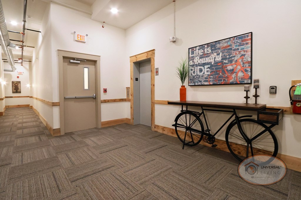 A hallway with a door leading to the staircase and an elevator with a bike-shaped table nearby.