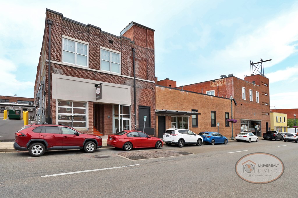 A line of cars parked in front of a historic brick apartment building along a downtown street.
