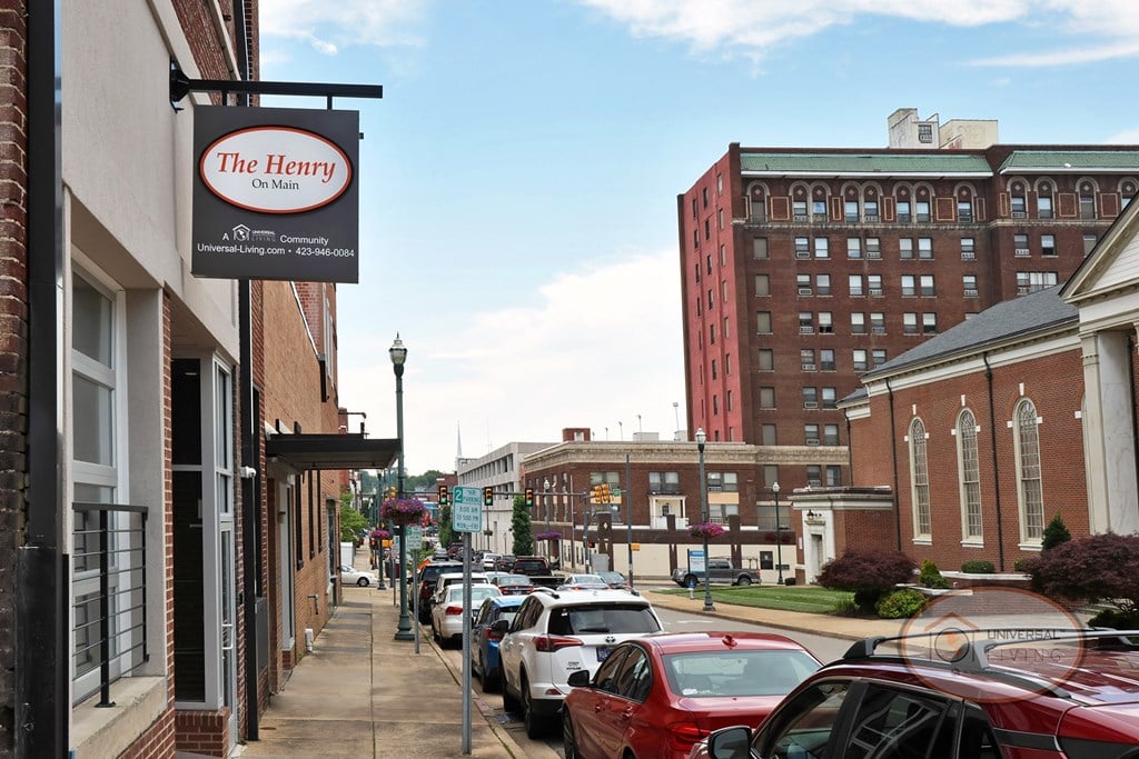A street vie of The Henry on Main property sign hanging off the side of a brick building with downtown Johnson City in the background.
