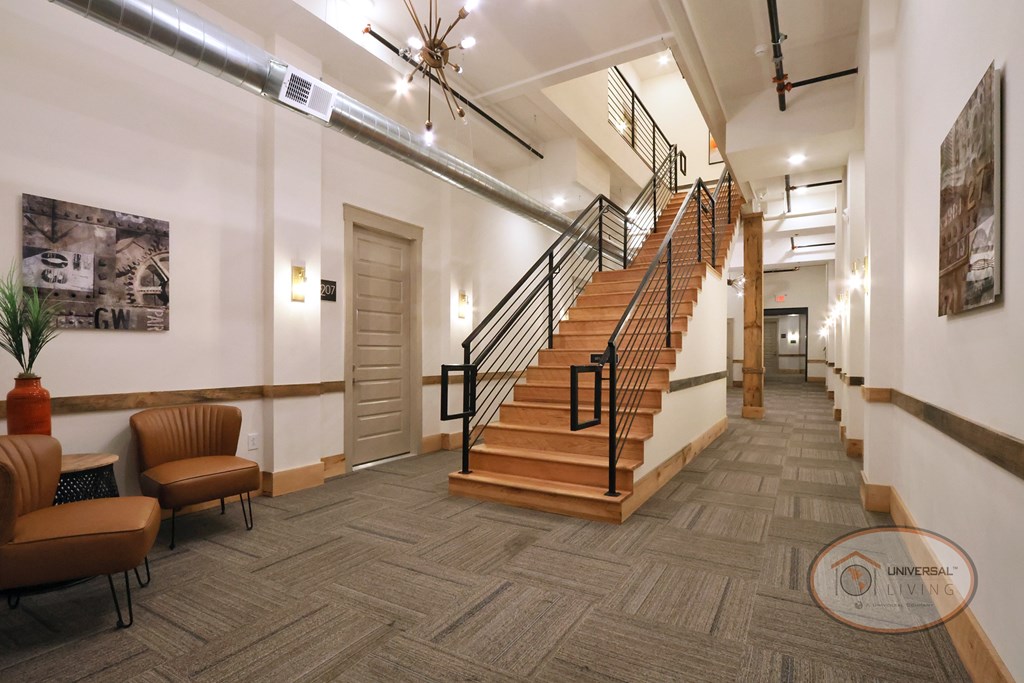 A hallway decorated with artwork, fine lighting fixtures, and a sitting area near a grand staircase.