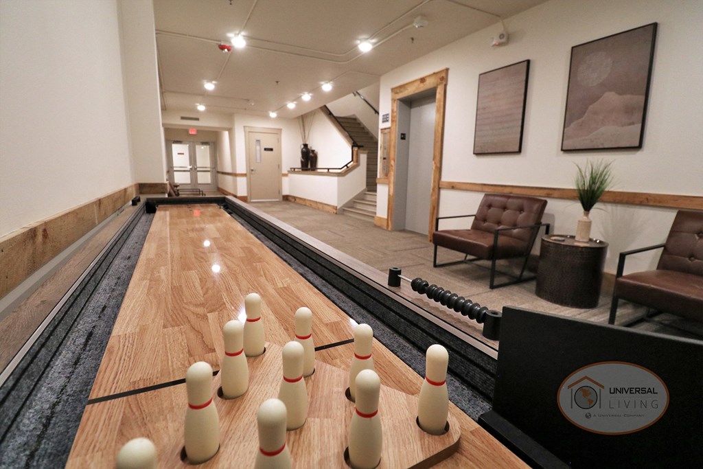 A close up photo of a shuffle board table with lounge seating, a stairwell, and an elevator in the background.