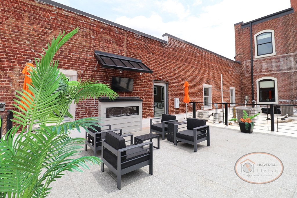A rooftop patio with fireplace, flat screen TV, lounge seating, umbrellas, and greenery.