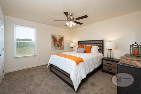 A bedroom with a queen size bed, carpet, and a ceiling fan.