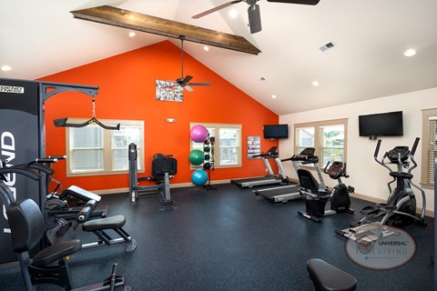 A gym with orange walls and a variety of exercise equipment with flat screen TVs.