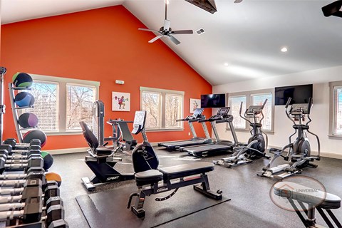 A gym with an orange accent wall and a variety of exercise equipment.