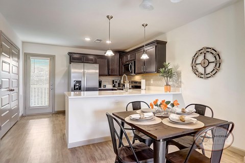 A kitchen with a table set for two with a clock on the wall.