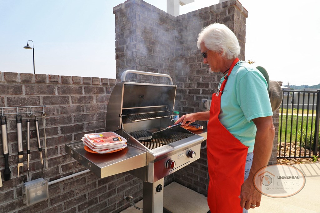 A man in an orange apron cooking burgers on the grill.