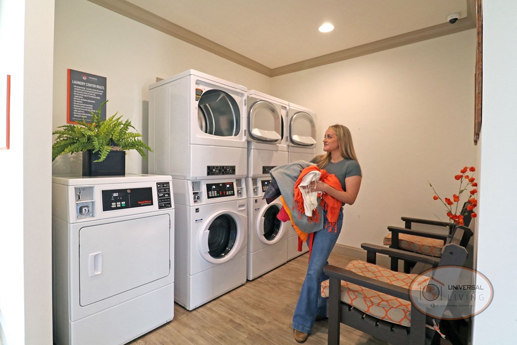 A woman holding an armful of laundry stands in front of an open washing machine.