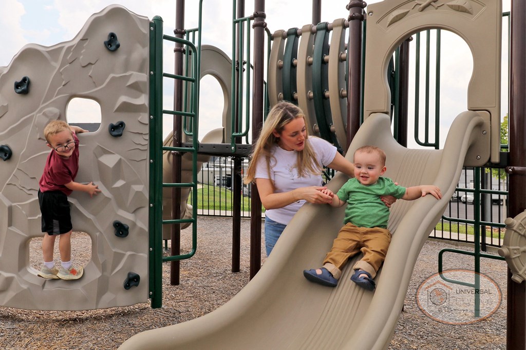 A mother and two children playing on a slide on a playground.