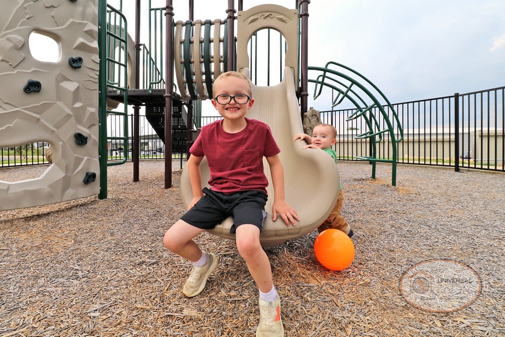 Two children sitting on a slide at a playground.