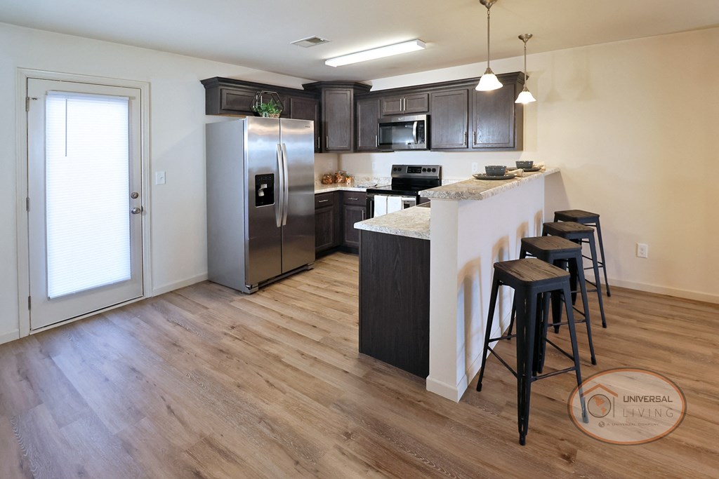 A kitchen with a refrigerator, stove, and bar stools.