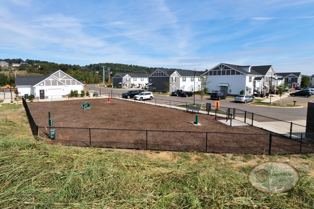 A landscape view of the fenced in dog park with obstacles, bench, and a water fountain for pets.