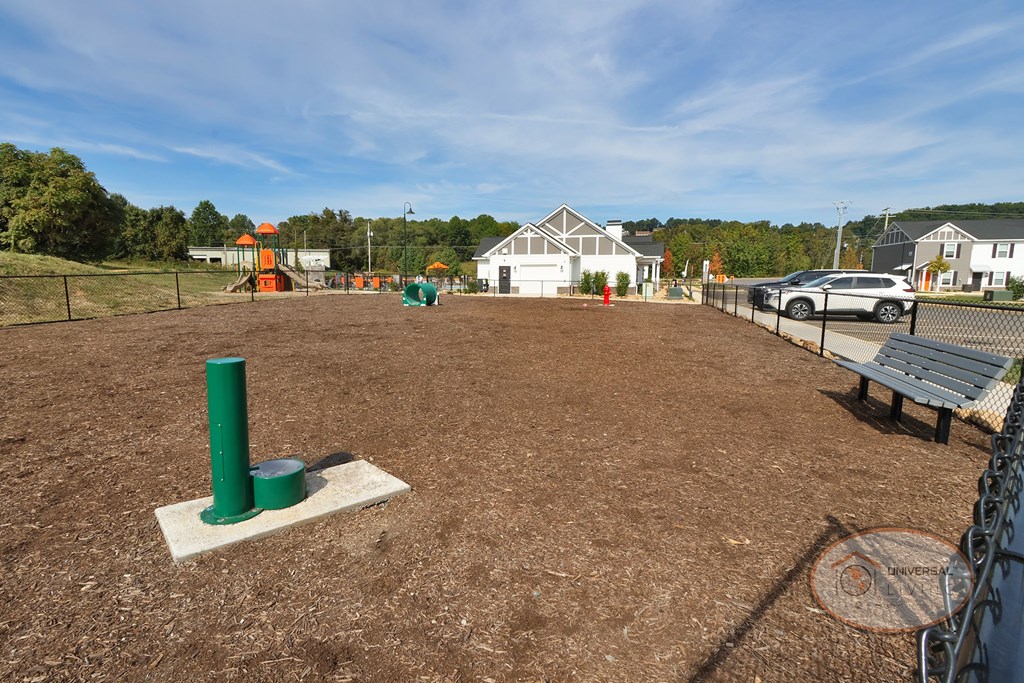 A close up of the fenced in dog park with bench, obstacles, and water fountain for pets.