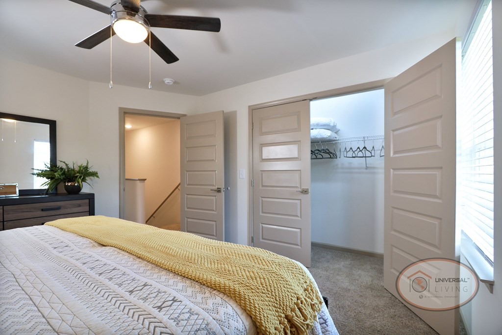 A bedroom with a bed, large walk in closet, and ceiling fan.
