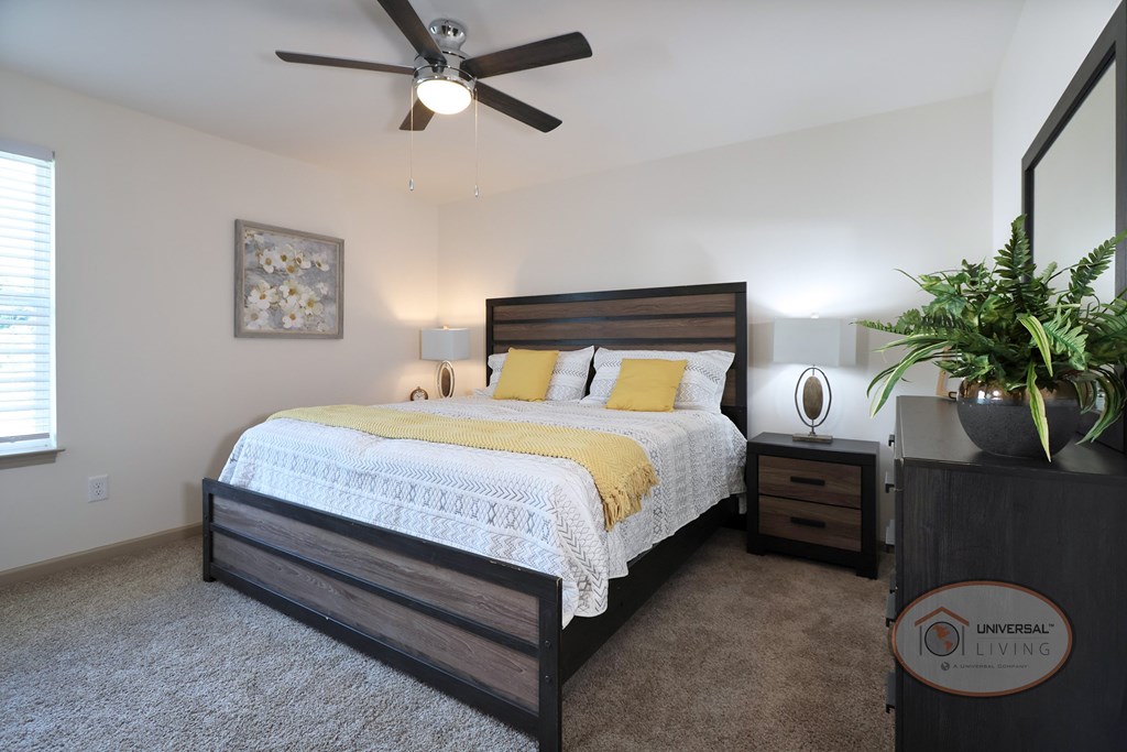 A bedroom with a bed, carpet, ceiling fan, and white walls.