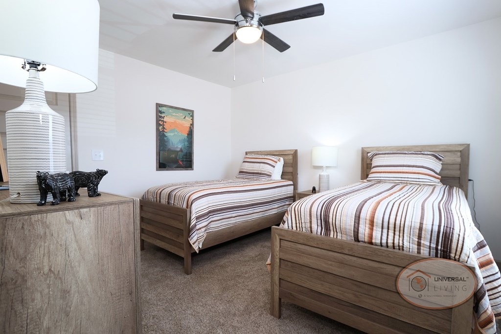 A bedroom with two twin beds, a ceiling fan, and carpet.