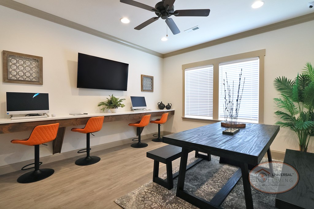 A business center with orange barstool seating, computers and free Wi-Fi, flat screen TV, large window, and table.