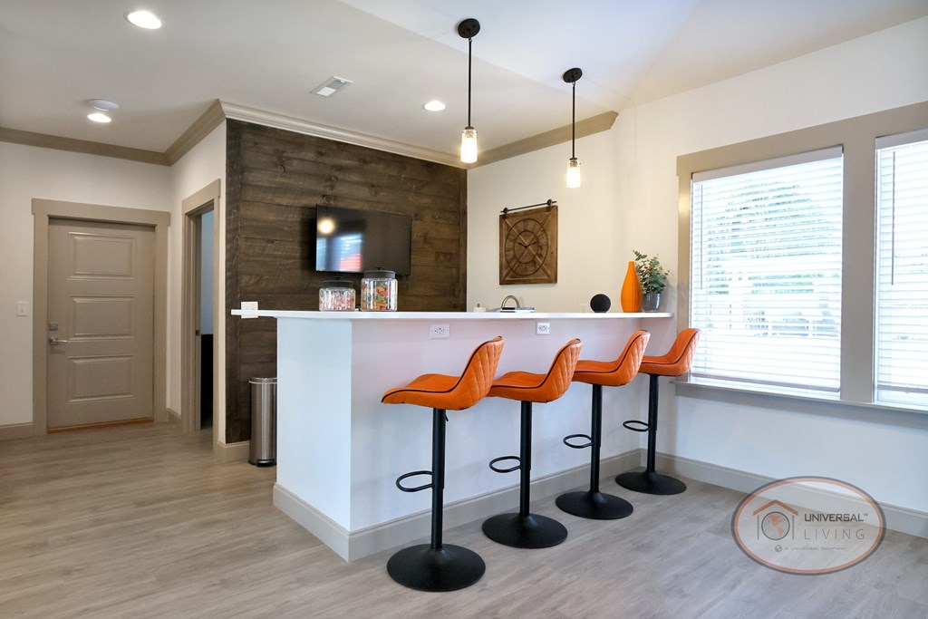 A coffee bar with orange barstool seating, a wooden accent wall, and flat screen TV.