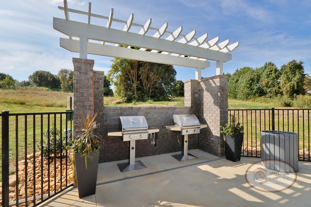 A white pergola is over two stainless steel barbecue grill.