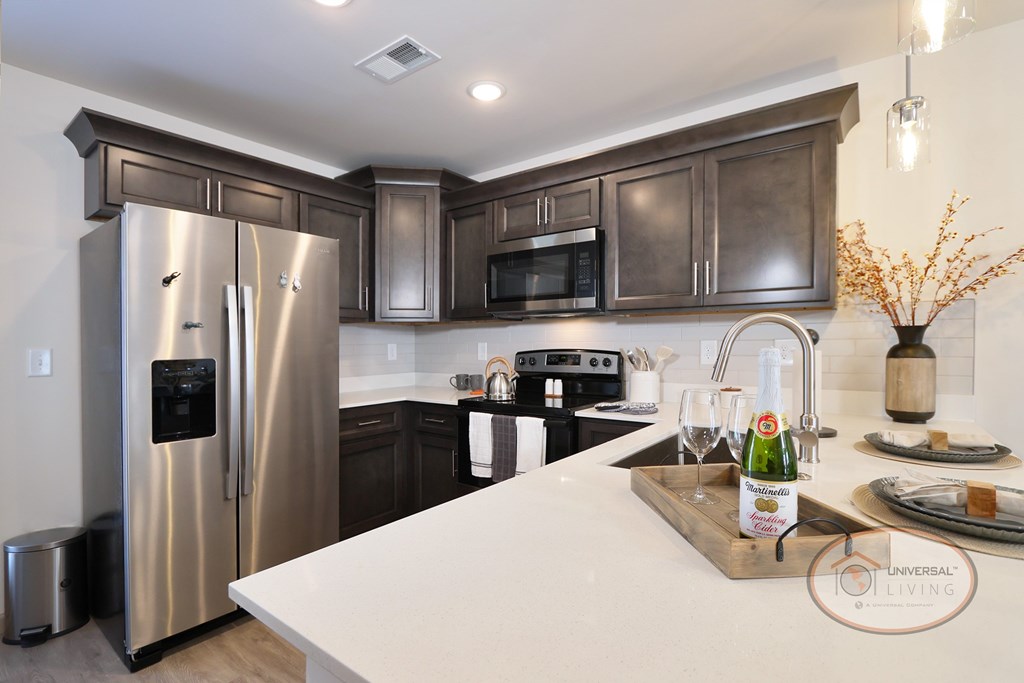 A kitchen with quartz countertops, stainless steel refrigerator and appliances, as well as dark brown cabinets.