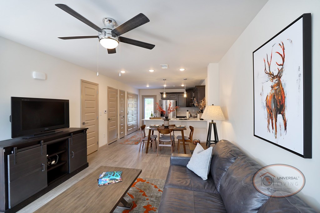 Another view of the furnished living area with hardwood vinyl flooring, white walls, with the kitchen and patio door visible in the background.