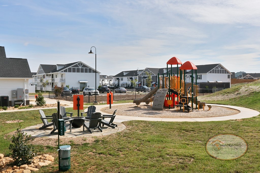 A landscape view of the playground and fire pit with white and grey apartment buildings in the background.