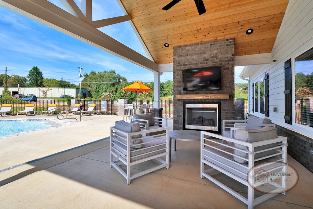 An outdoor pavilion with lounge seating, fireplace, flat screen TV, and ceiling fan.