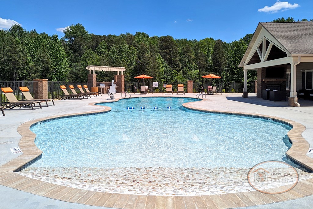 A resort style saltwater swimming pool with zero entry, lounge chairs, grills, and the clubhouse in the bakground.