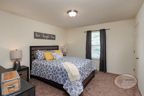 A bedroom with a large bed, carpet, white walls, and a large window.