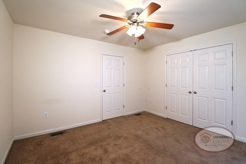 A bedroom with a large closet, carpet, white walls, and a ceiling fan.