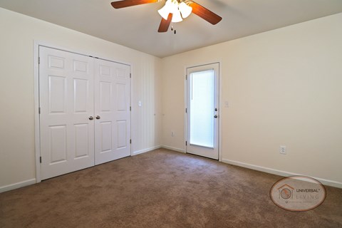A bedroom with a large closet, carpet, white walls, a ceiling fan, and a glass door leading to the balcony.