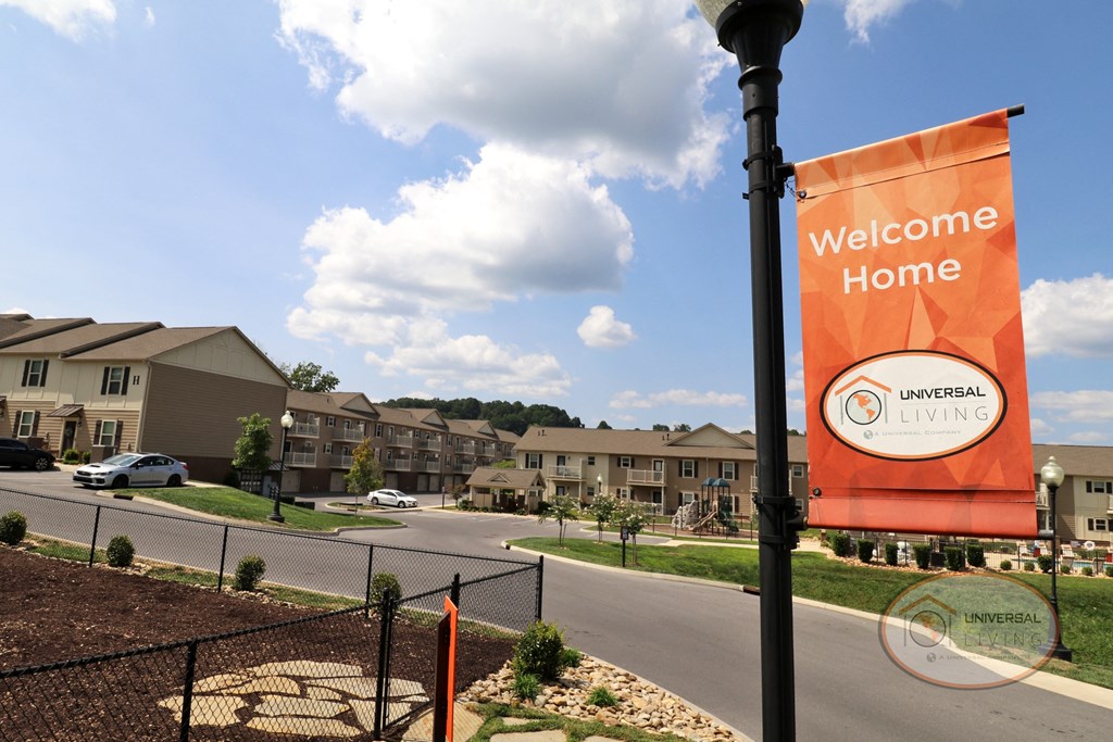 A sign that reads welcome home in front of an apartment building.